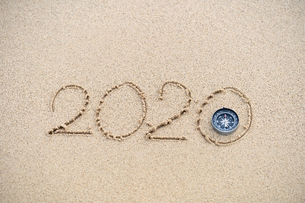 The number 2020 is written in the sand with a compass laying within the last 0, providing direction during an unprecedented year.